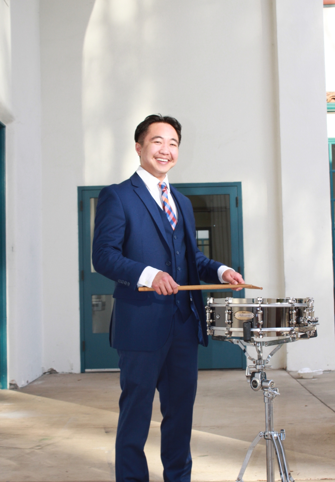 Allen Daniel Rivera playing drums in a suit outdoors