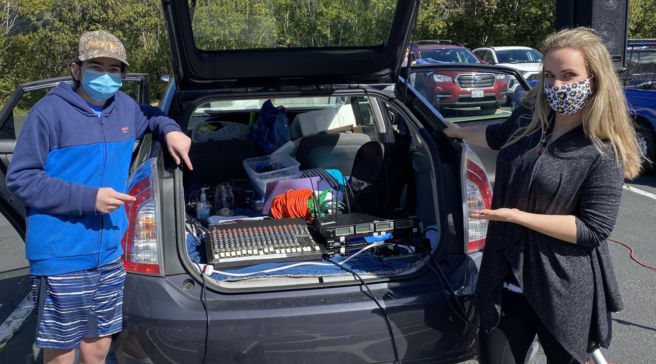 Ashley Kimball and a young man standing by the trunk of her car with sound equipment and speakers
