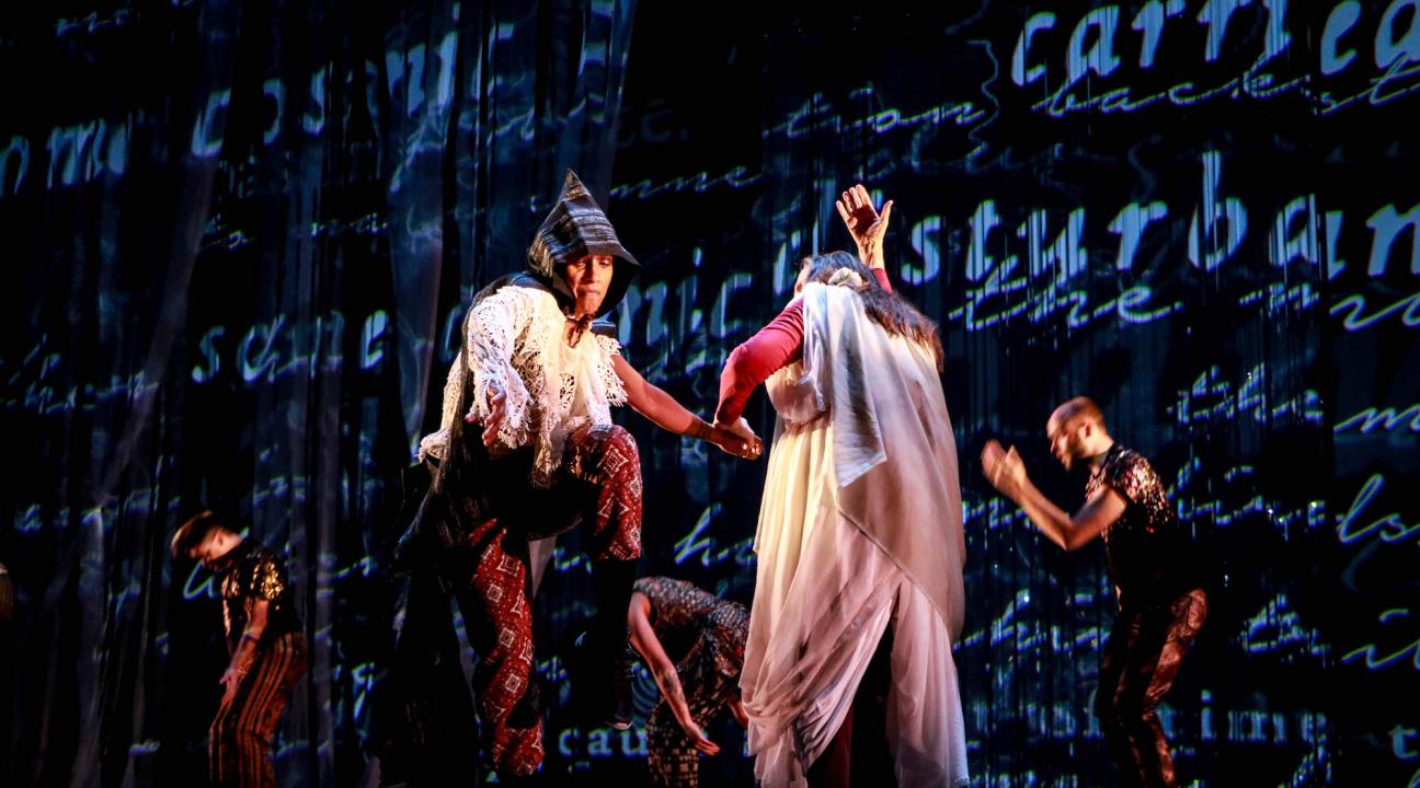 Dancers in costume in front of wall with word projections