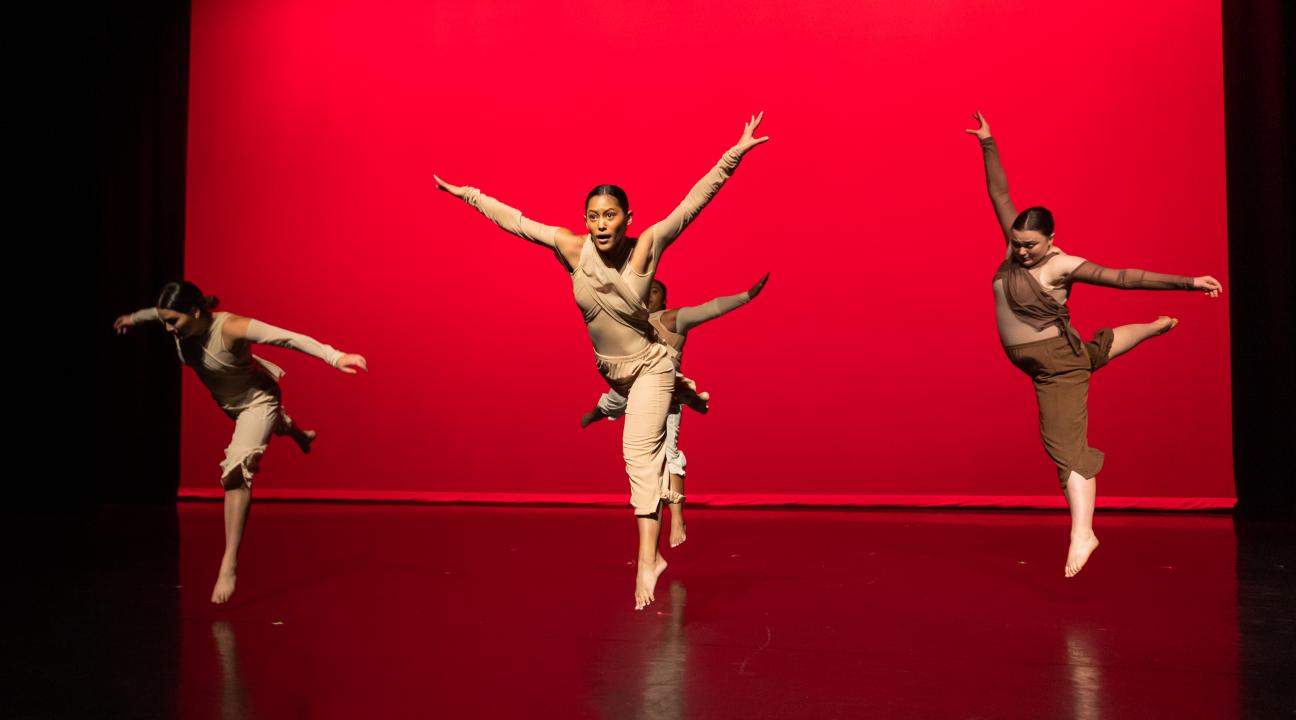 Dancers jumpin in the air with arms extended against a red background