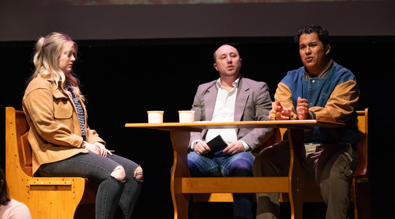 Three actors sitting at a table on stage