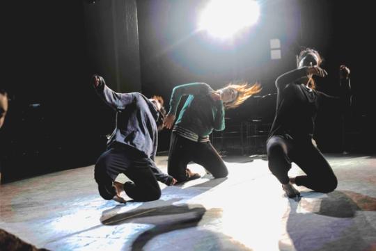 three dancers leading to the side with a bright light above them