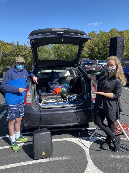 Ashley Kimball and a young man standing by the trunk of her car with sound equipment and speakers