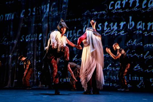 Dancers in costume in front of wall with word projections