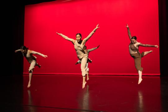 Dancers jumpin in the air with arms extended against a red background