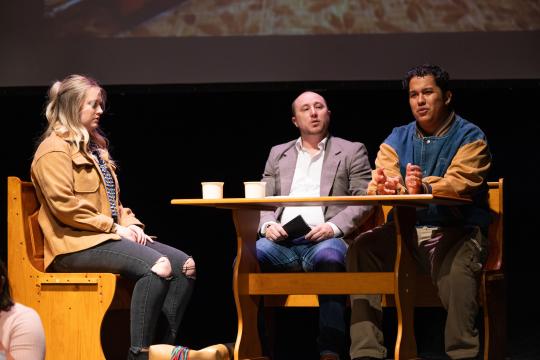 Three actors sitting at a table on stage