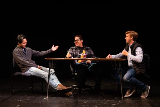 Three actors sitting around table on stage